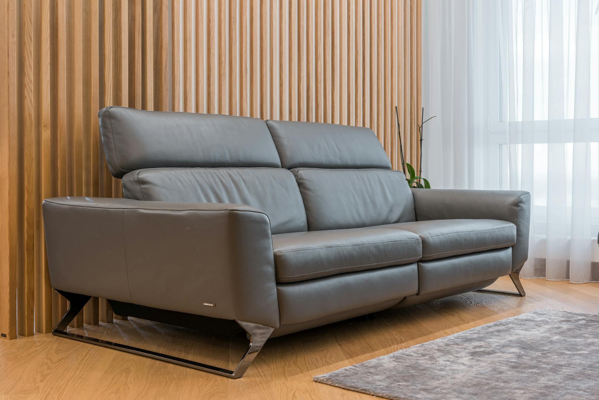 Large gray leather sofa placed in living room with carpet and windows with white curtains